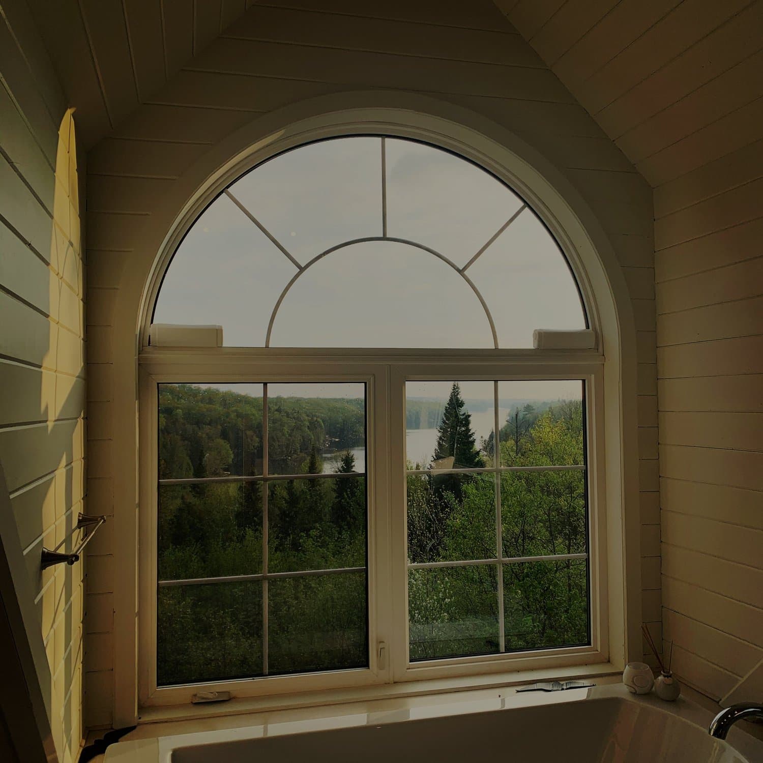 Arched bathroom window with a forest view